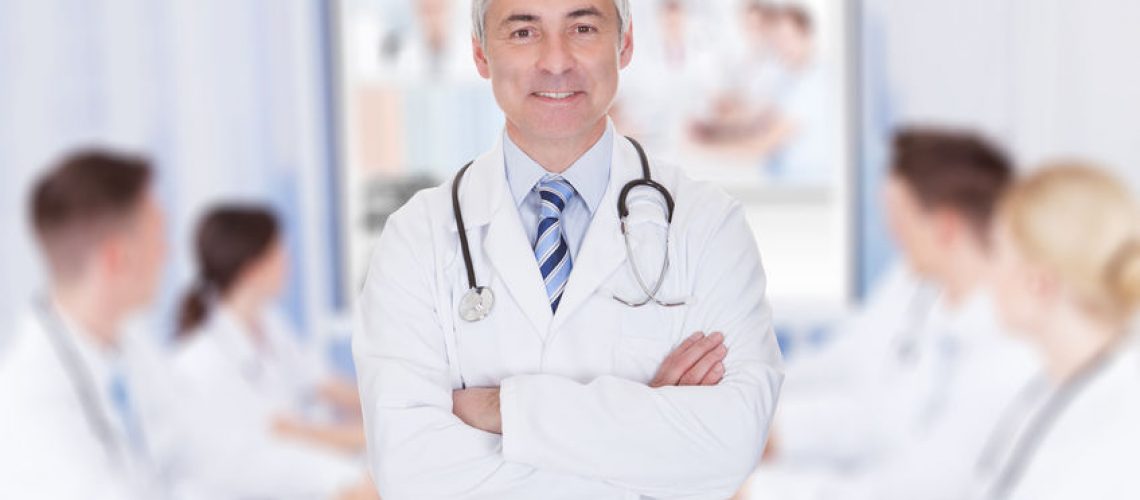 33846550 - portrait of senior doctor with arms crossed against team video conferencing in meeting room