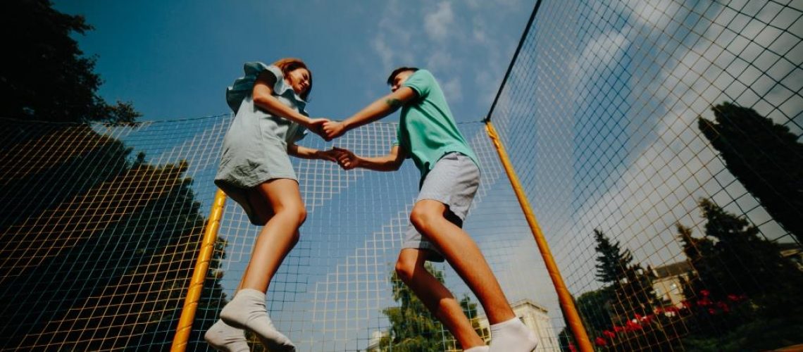 couple-jumping-on-trampoline-in-the-park-PKP3F37